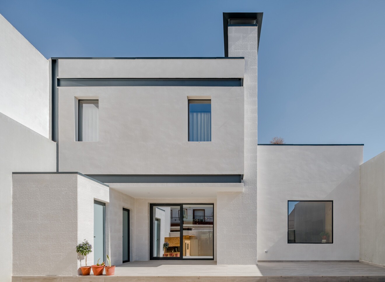 Fachada moderna de vivienda unifamiliar con revestimiento blanco y ventanas estrechas.