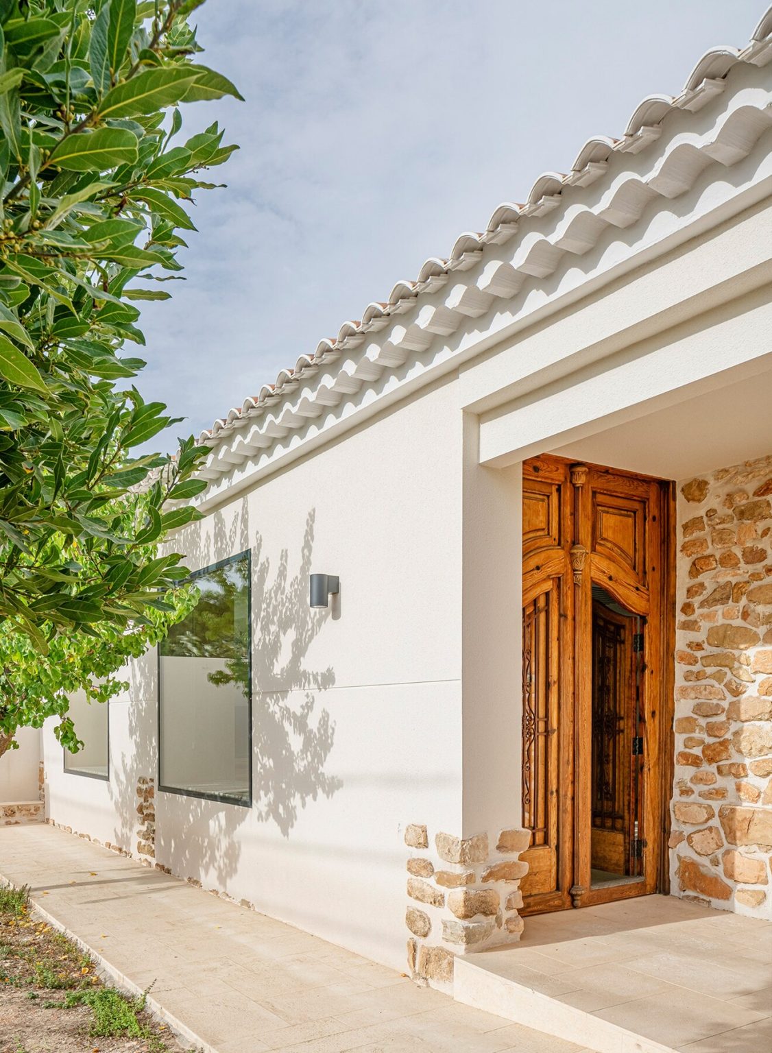 Detalle de la entrada de una casa de campo con puerta de madera y fachada blanca.