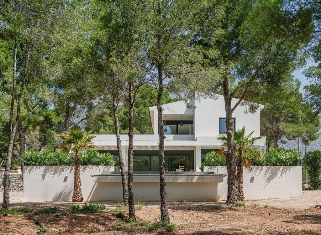 Fachada de una vivienda moderna rodeada de pinos en un entorno natural.