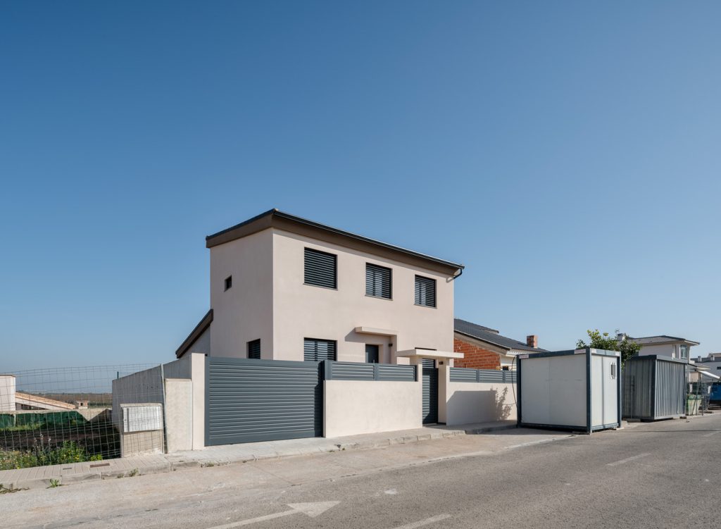 Vivienda unifamiliar moderna con fachada blanca y cerramiento metálico.